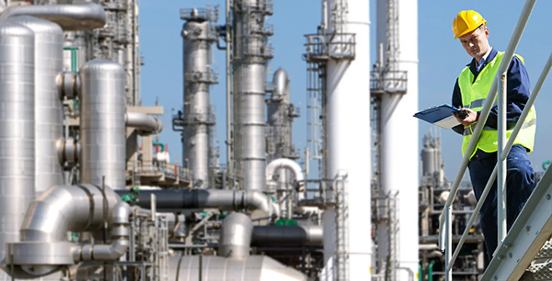 Shutterstock _77496391-A Petrochemical Engineer With A Noteboard In His Hand In Front Of A Huge Refinery